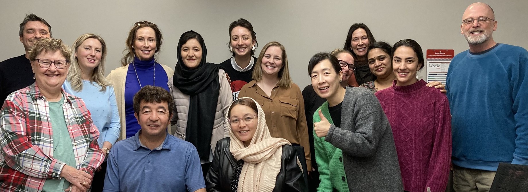 A diverse group of adults posing and smiling together in a classroom setting, with some sitting and others standing behind them.